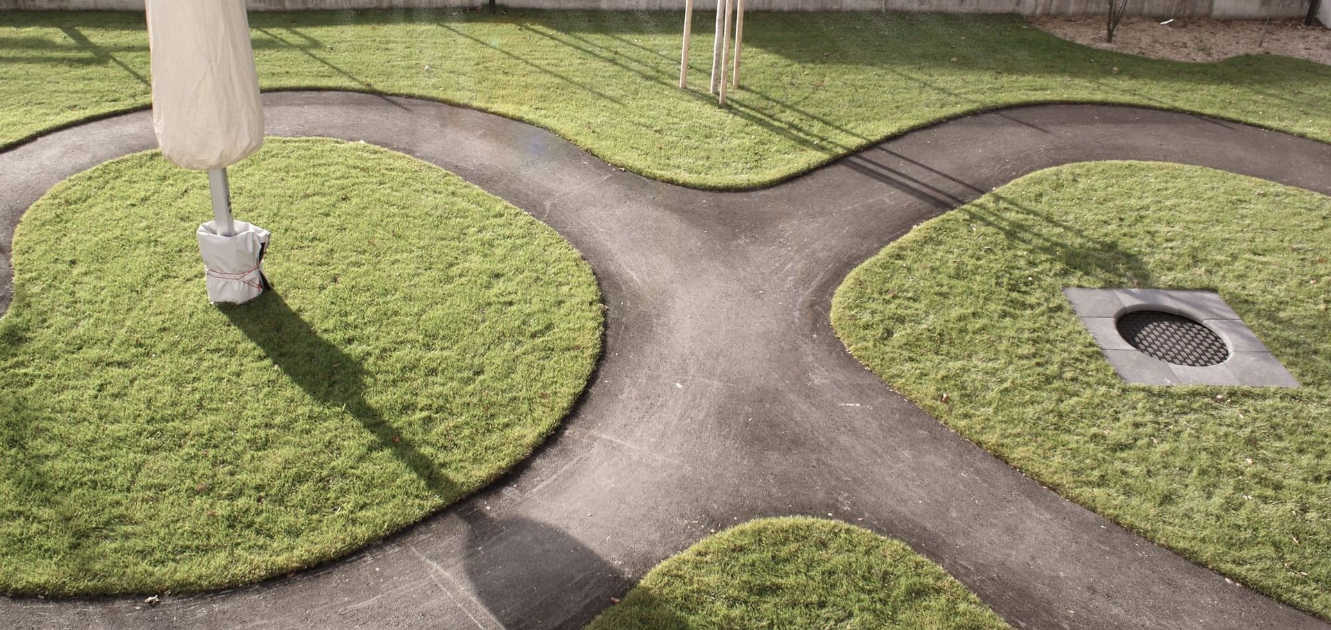 Luftaufnahme von verschlungenen Wegen zwischen Grasflächen mit dem Schatten eines Laternenpfahls