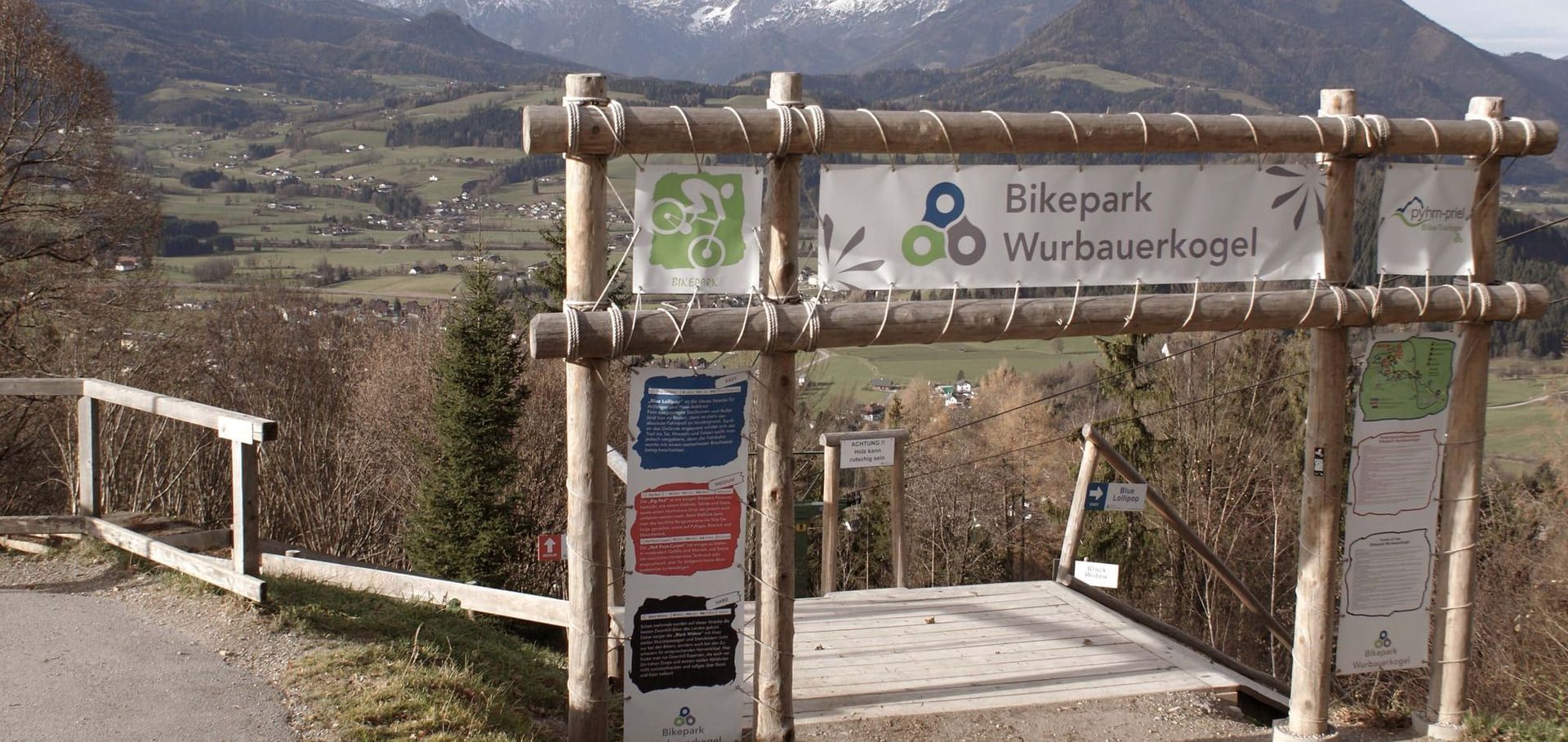 Mit Holzbalken umrahmte Einfahrt zum "Bikepark Wurbauerkogel" mit malerischer Tal-Kulisse