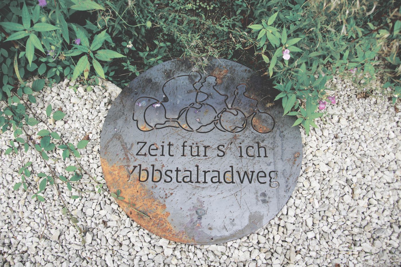 Schild mit dem Schriftzug "Ybbstalradweg - Zeit fürs ich" auf einem Kiesbett