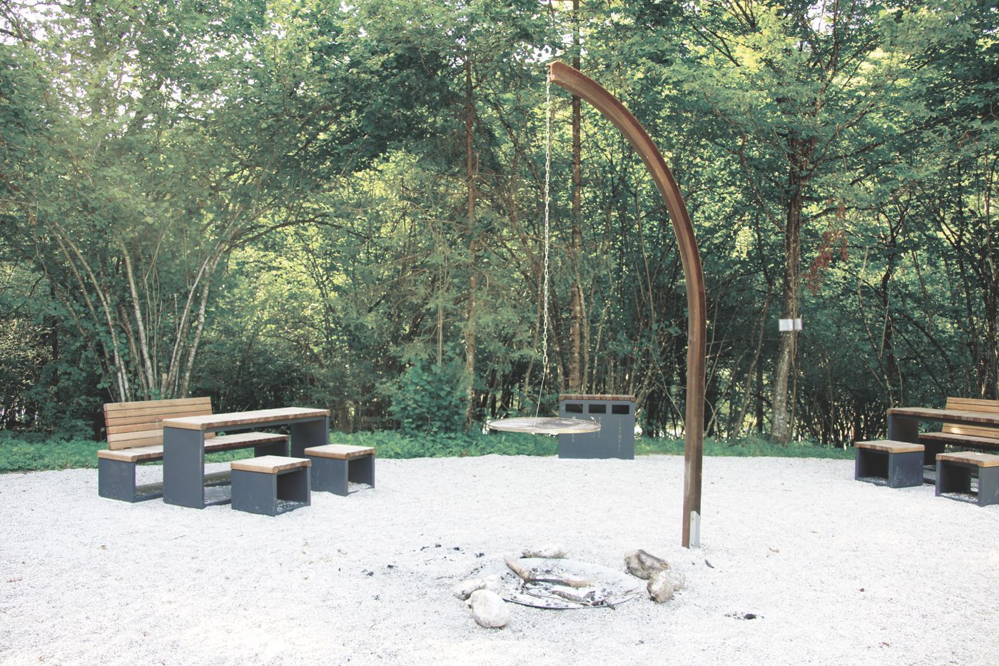 Freie Feuerstelle mit modernen Möbeln aus Stahlquadern mit Holzplanken auf einer Waldlichtung
