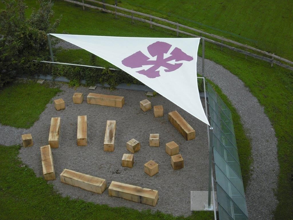 Luftaufnahme von kreisförmig angeordneten Holzbänken unter einem großen weißen Baldachin mit einem violetten Emblem