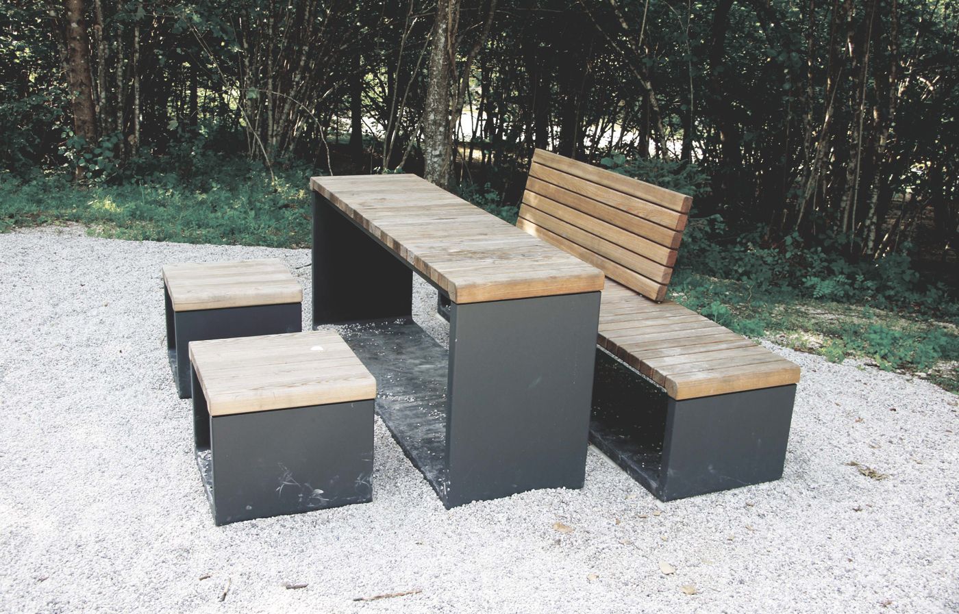 Moderne Möbel aus Stahlrahmen mit Sitzflächen und Tischplatten aus Holz in einem Kiesbett in einem Wald